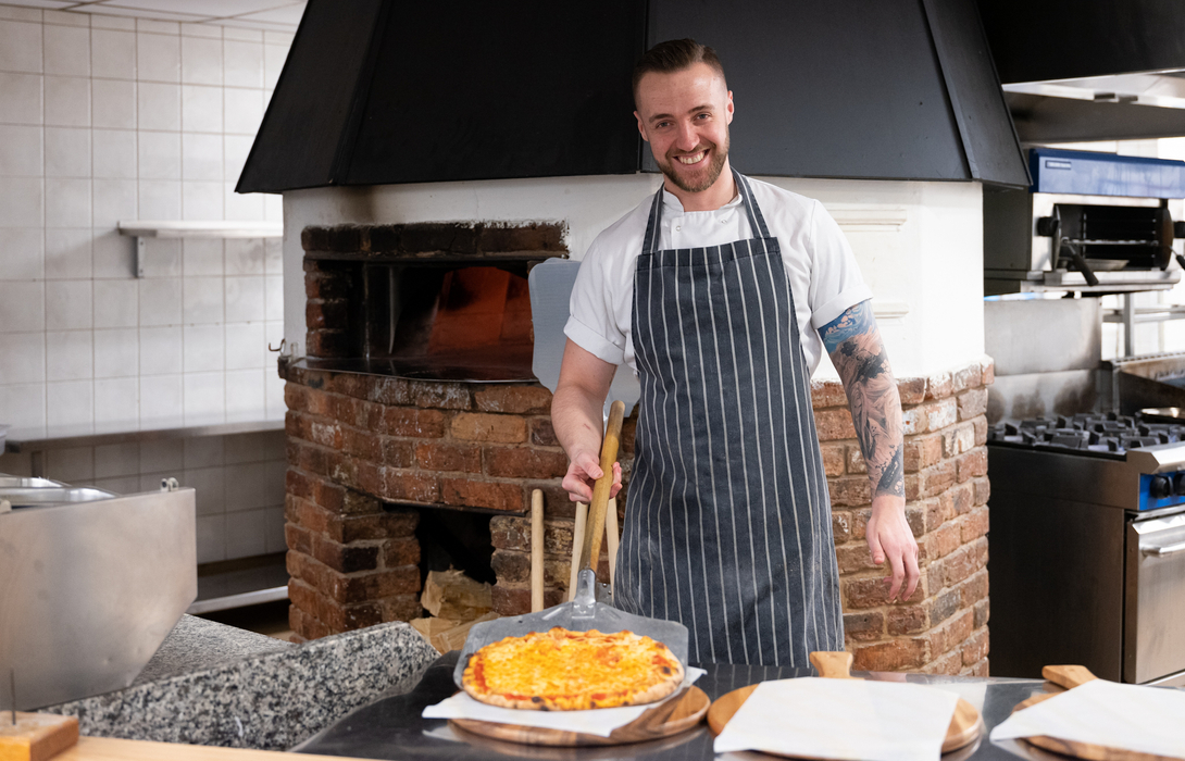 Chef showing off pizza he made in a pizza oven