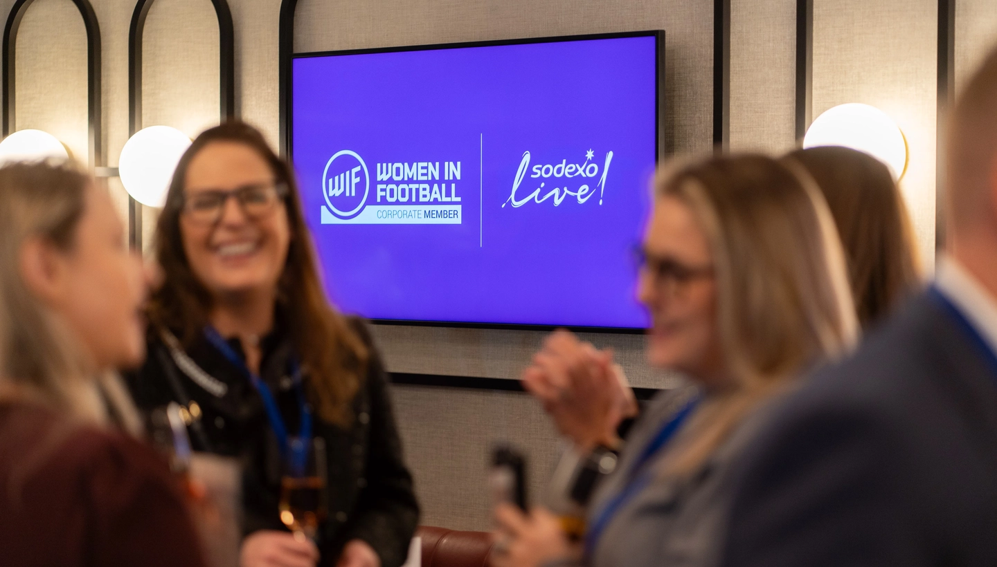 Women gather around TV displaying Women In Football and Sodexo Live!