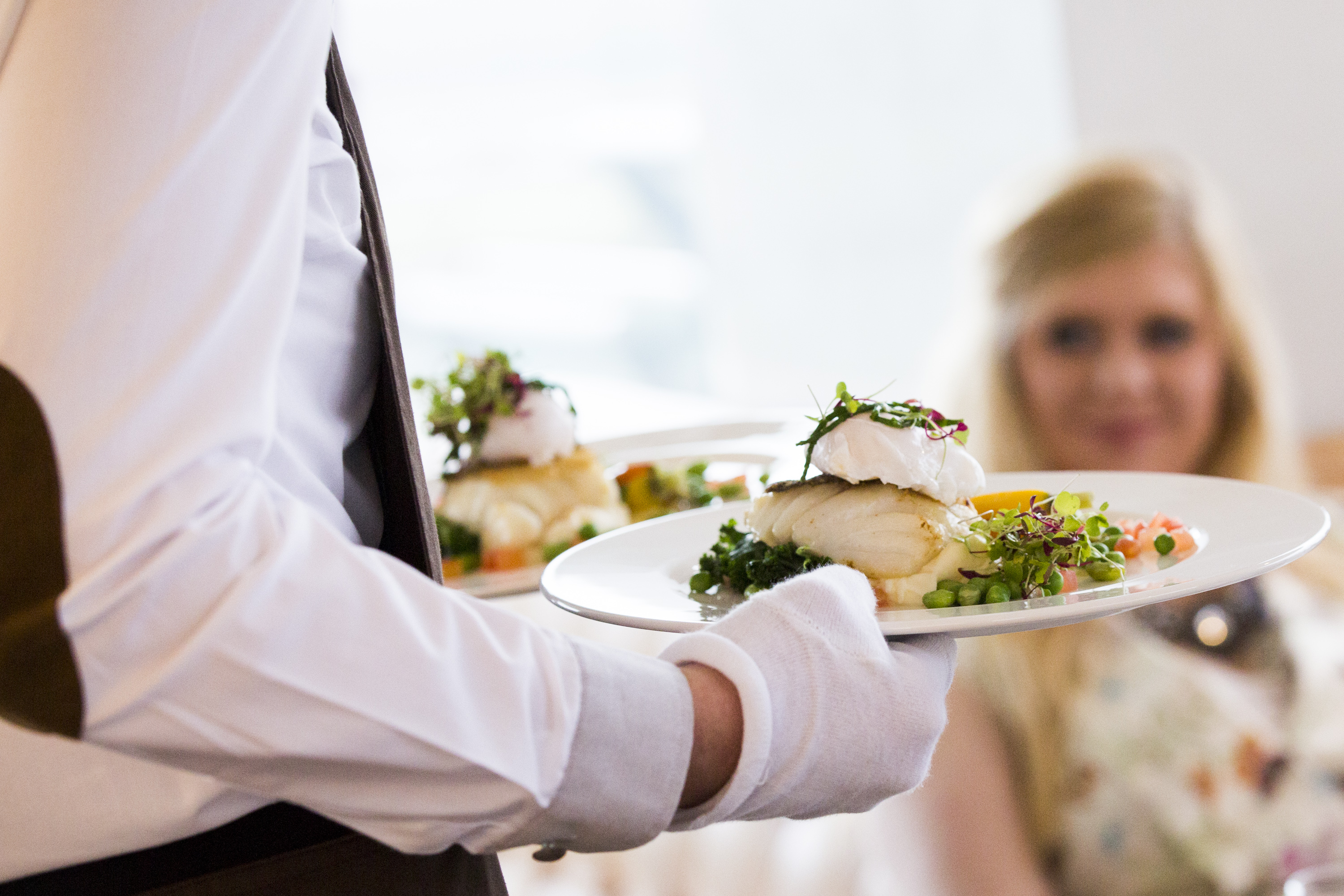 Waiter handing fish and peas on a plate to a woman