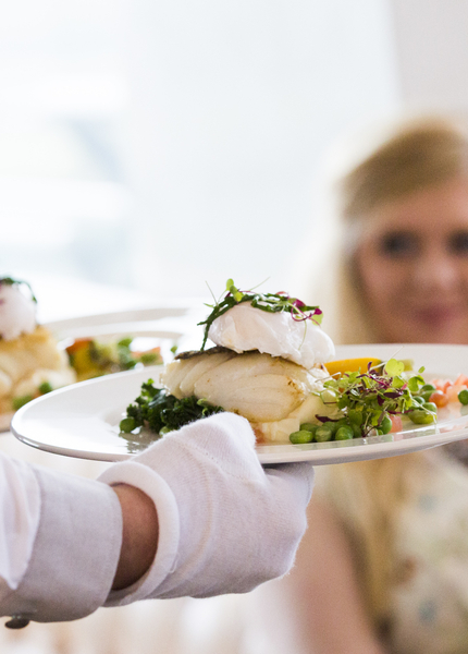 Waiter handing fish and peas on a plate to a woman