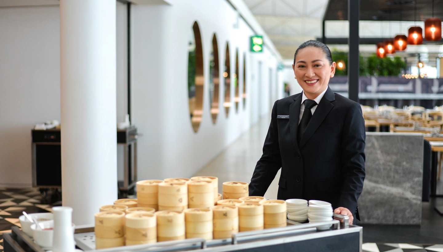 A smiling waitress pushing a food wagon in Hong-Kong International Airport