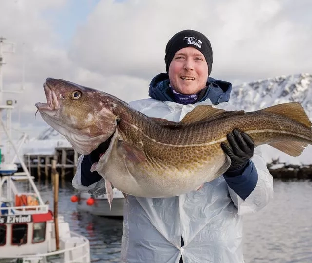 Man holding a fish he caught with the Norwegian icy waters in the background
