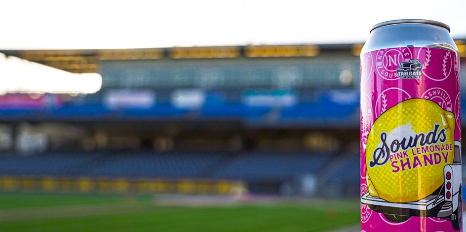 Woman holding can of Shandy on baseball field